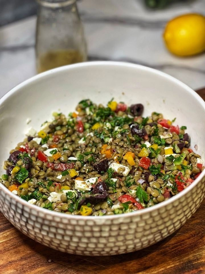A large bowl filled with lentil salad. This easy lentil salad contains tomatoes, cucumbers, feta cheese and fresh herbs.