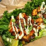 One blackened salmon lettuce wrap on a piece of brown parchment paper garnished with fresh salsa and homemade avocado lime crema