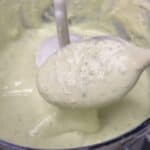 Avocado lime crema displayed on a spoon coming out of a food processor