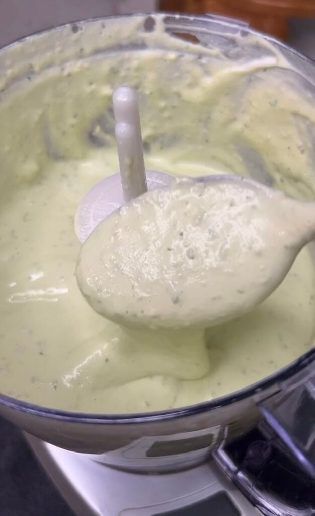 Avocado lime crema displayed on a spoon coming out of a food processor