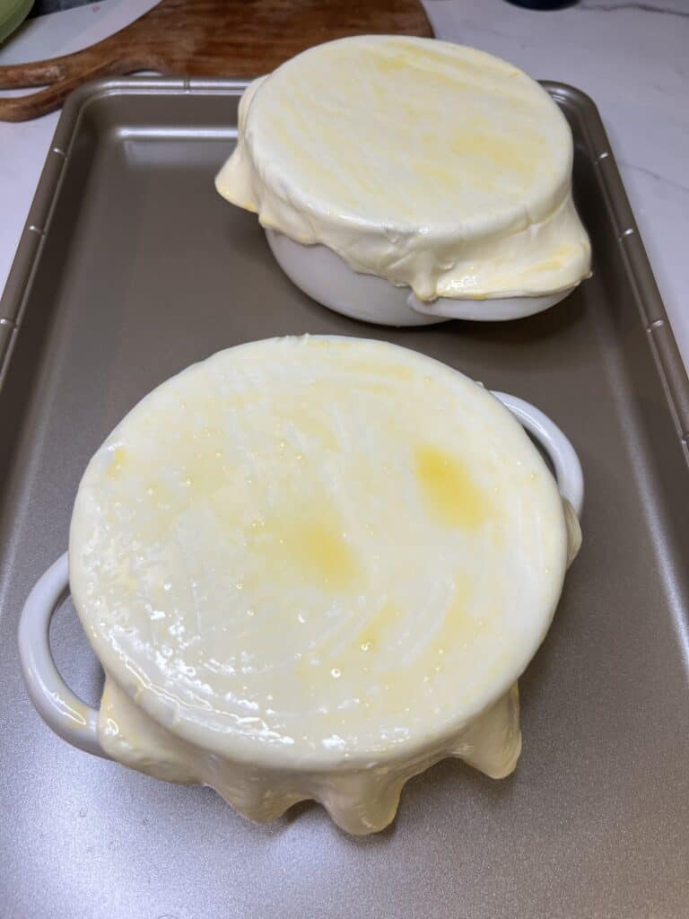 Puff pastry dough brushed with egg waas stretched over two white bowls of beef stew