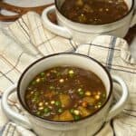 a white crock bowl filled with hearty beef stew with another filled crock in the background