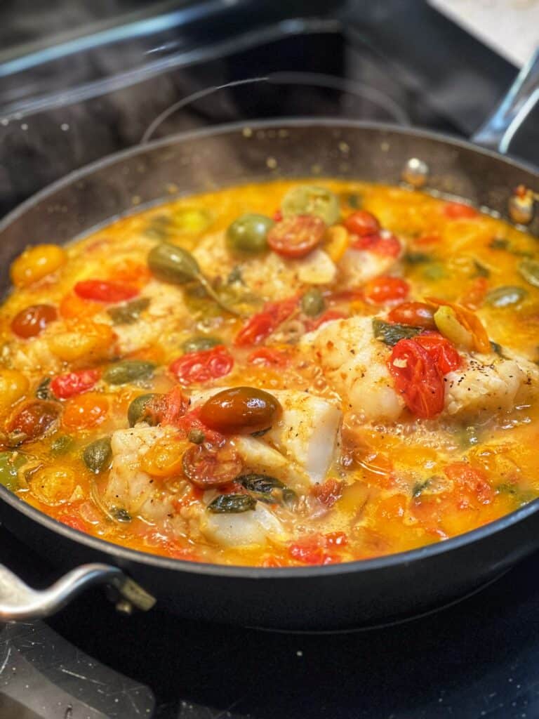 Four pieces of cod poached in a tomato poaching liquid.