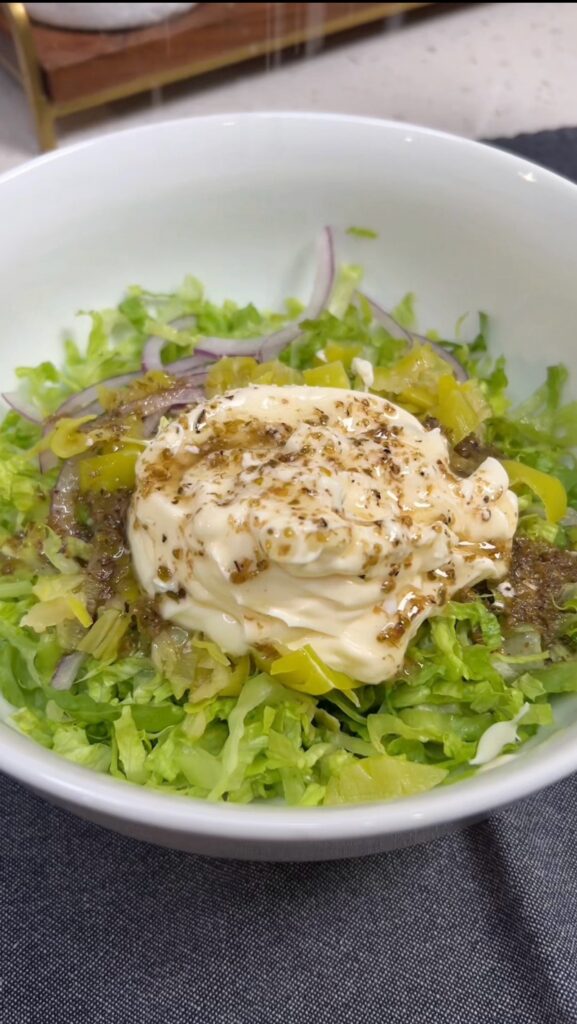 A bowl of shredded lettuce, thinly sliced red onion, chopped pepperoncini, mayo and submarine sauce.