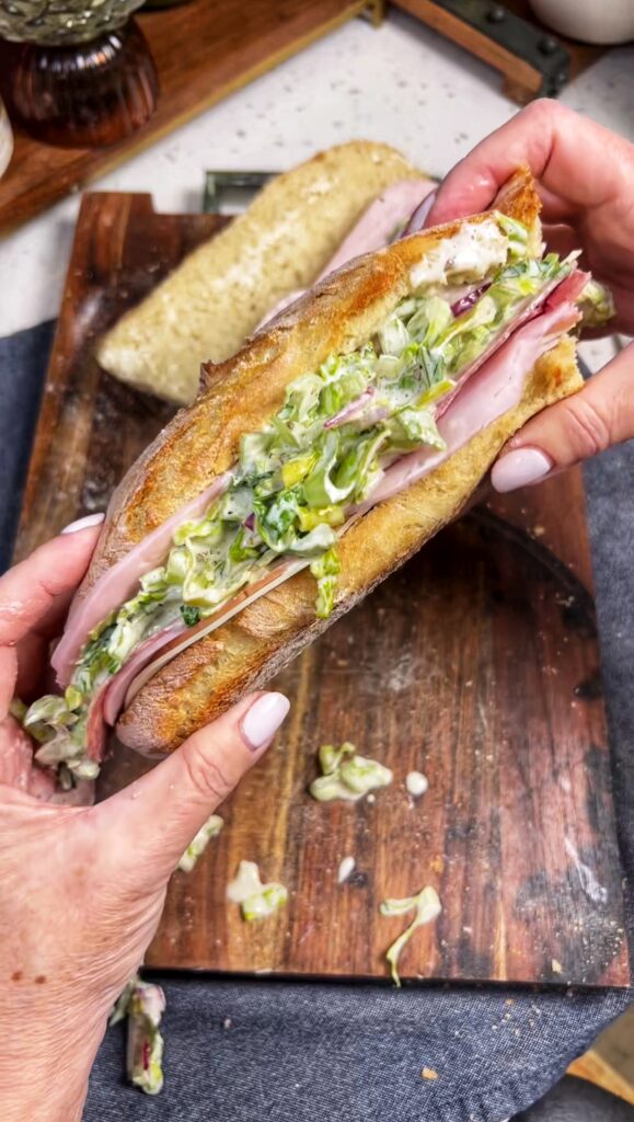 Me holding an Italian Grinder Sandwich. It's a baguette filled with deli meats, cheese and a creamy salad mixture.