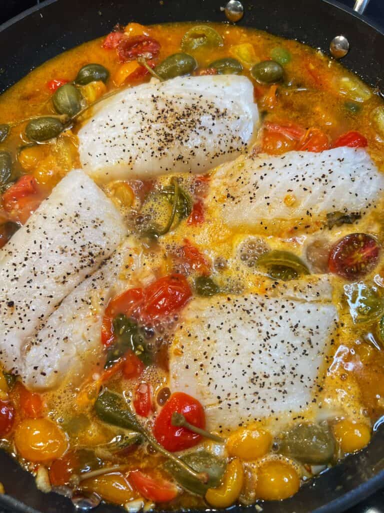 Cod filets placed in a tomato poaching liquid.