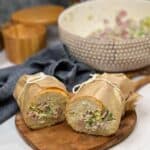 An Italian chopped grinder hoagie wrapped in brown parchment paper, cut in half and both halves tied with kitchen twine sitting on a small wooden cutting board.