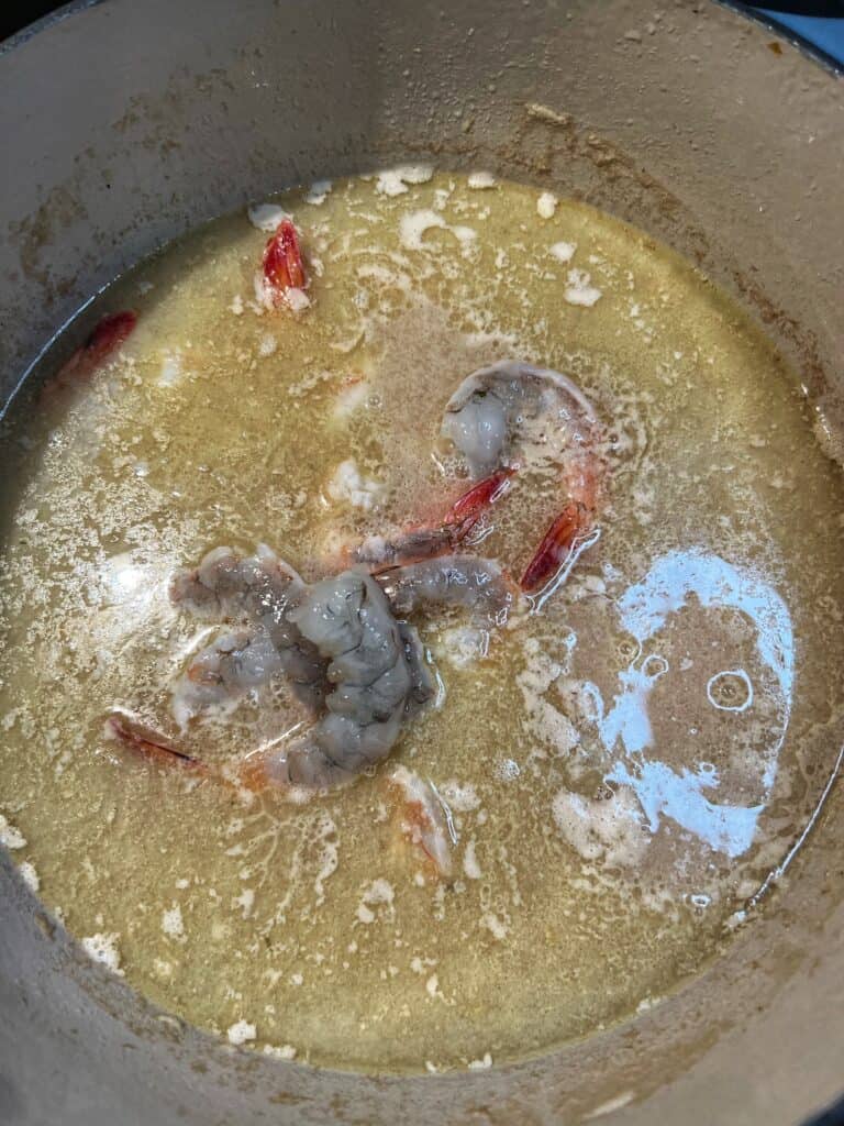 Raw, tail-on jumbo shrimp starting to poach in poaching liquid.