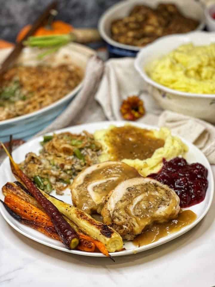A plate of Thanksgiving dinner with turkey roulade, mashed potatoes, orange cranberry relish, stuffing and roasted carrots