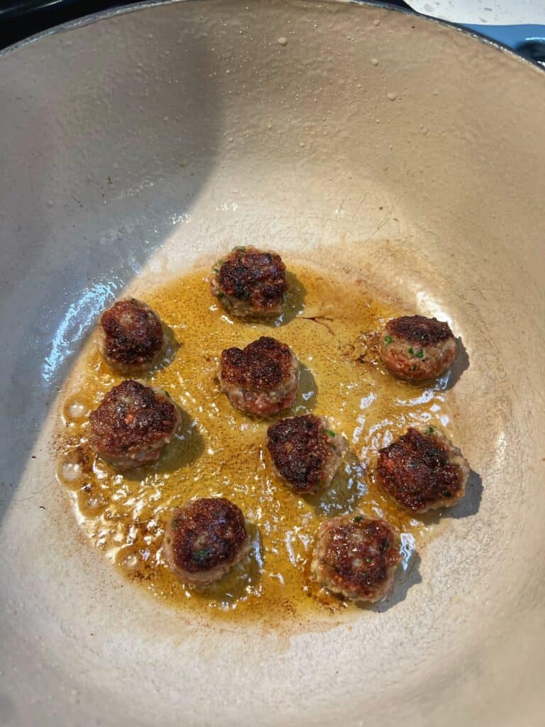 Nine mini meatballs browned in a deep pot.