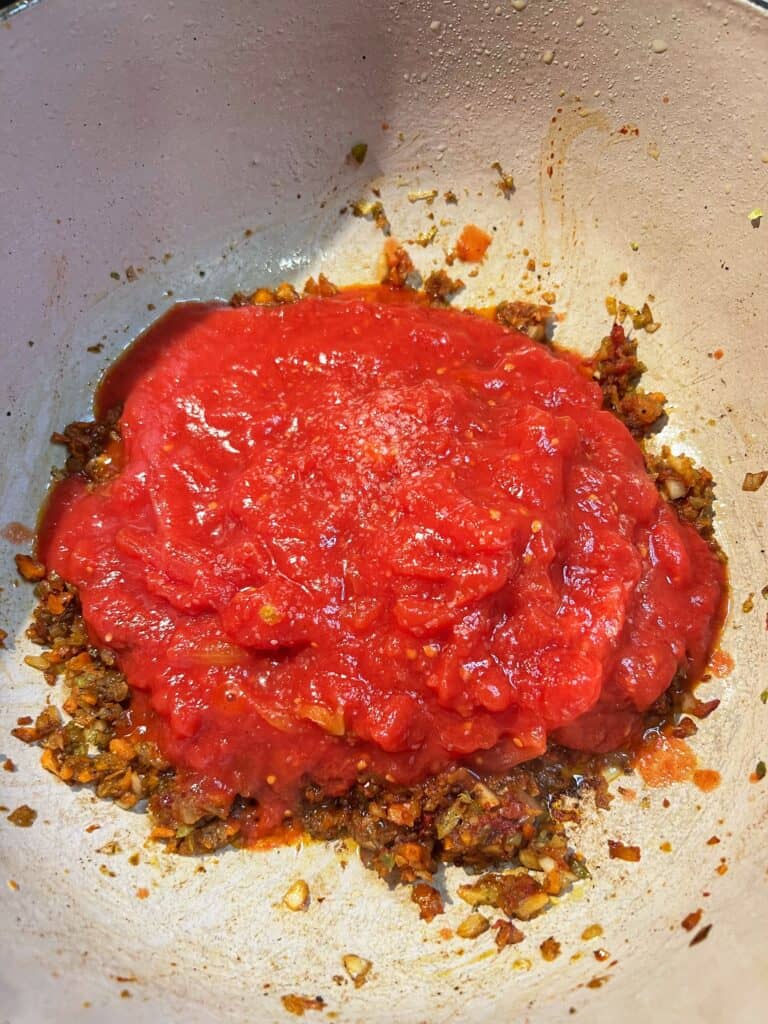 Crushed tomatoes added to a pot of sautéed vegetables and tomato paste.