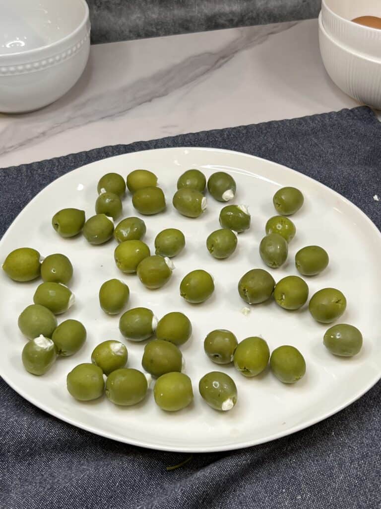 A white platter of green olives stuffed with cheese.