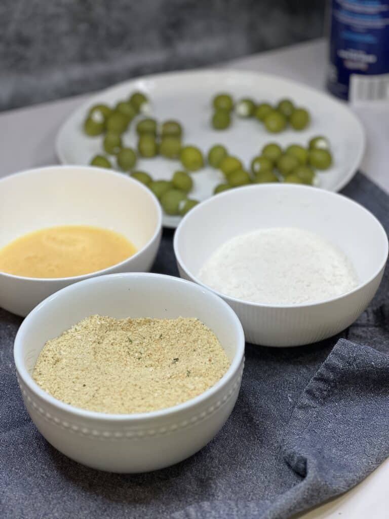 A dredging station for frying green olives. One white bowl contains flour, the other beaten eggs and the last holds a breadcrumb mixture.