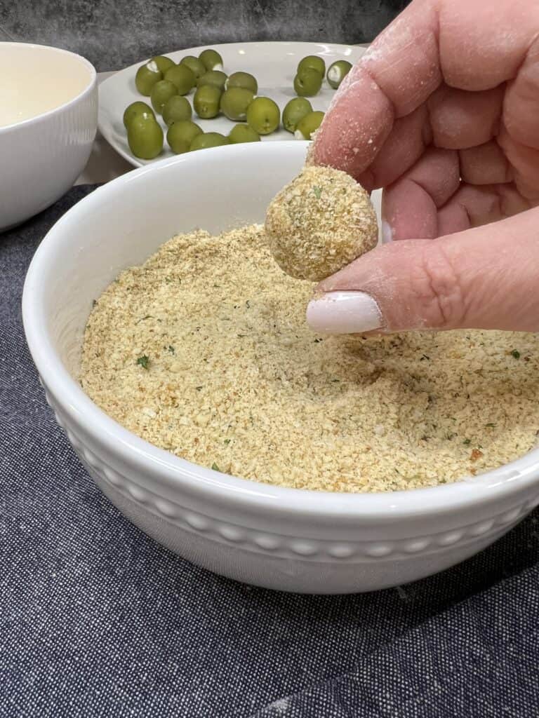 Me holding up one breaded olive over a bowl of breadcrumbs.