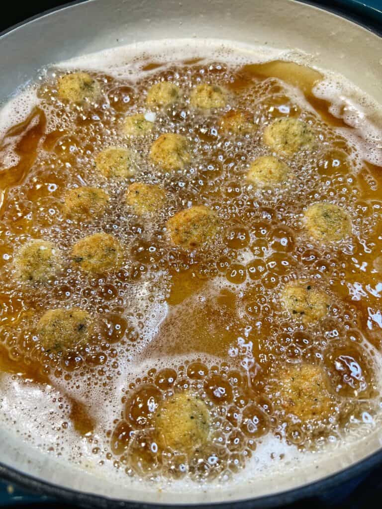 Breaded olives frying in a pan of oil.