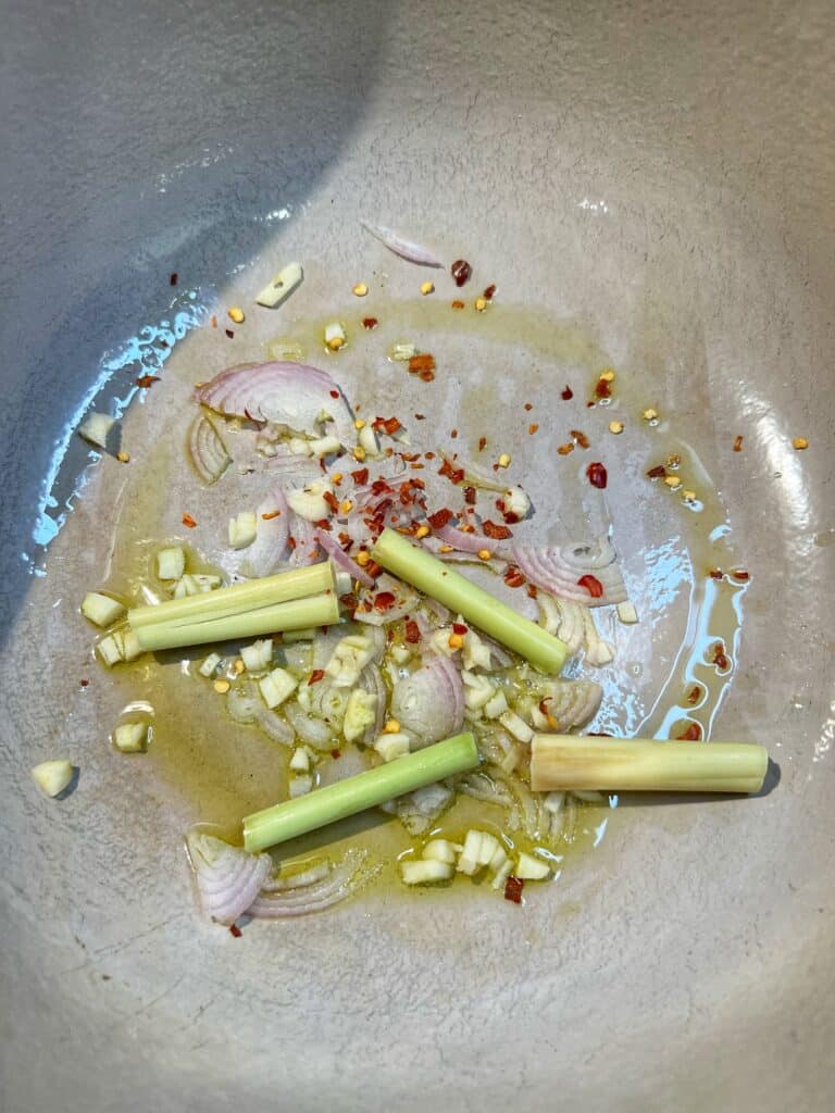 Sliced shallots, minced garlic, roughly chopped lemongrass and crushed red pepper sautéing in a large pot with a touch of heated olive oil.