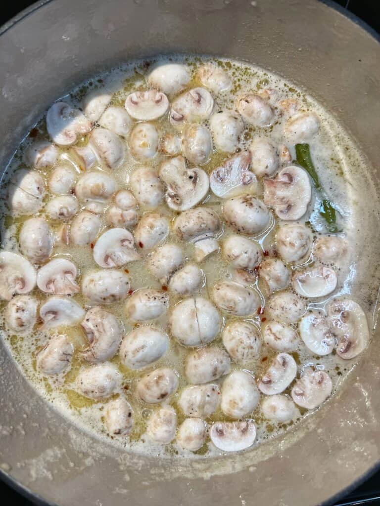 Raw, halved button mushrooms in a pot of simmered coconut broth.