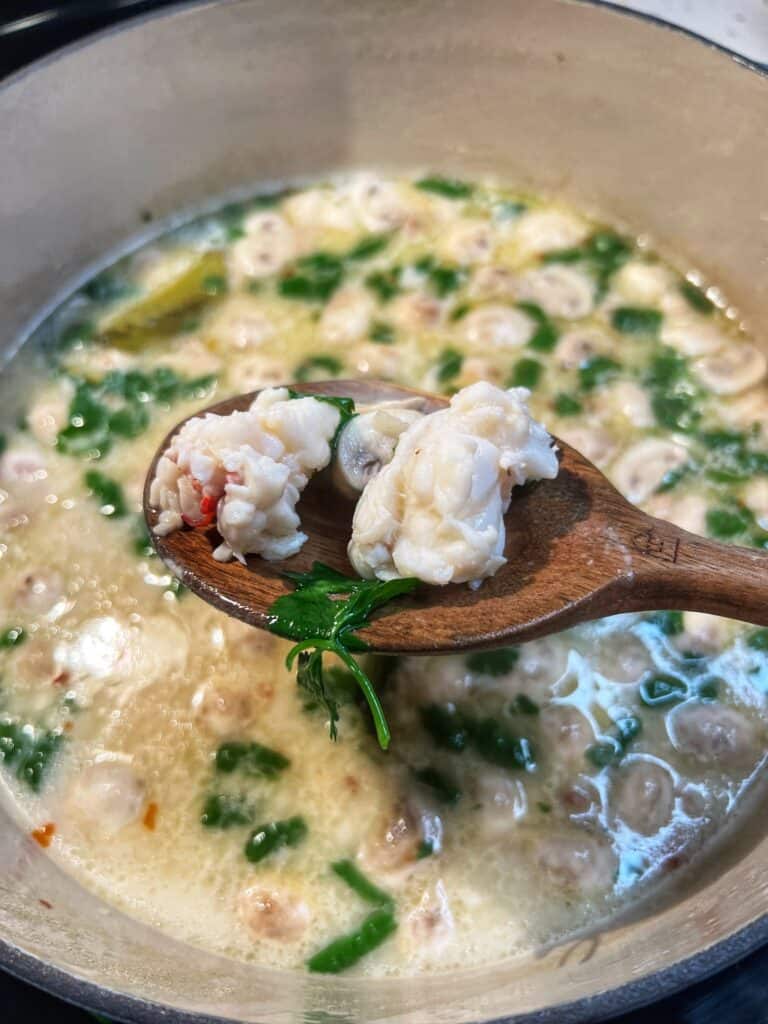 A wooden spoon holding two pieces of poached lobster.