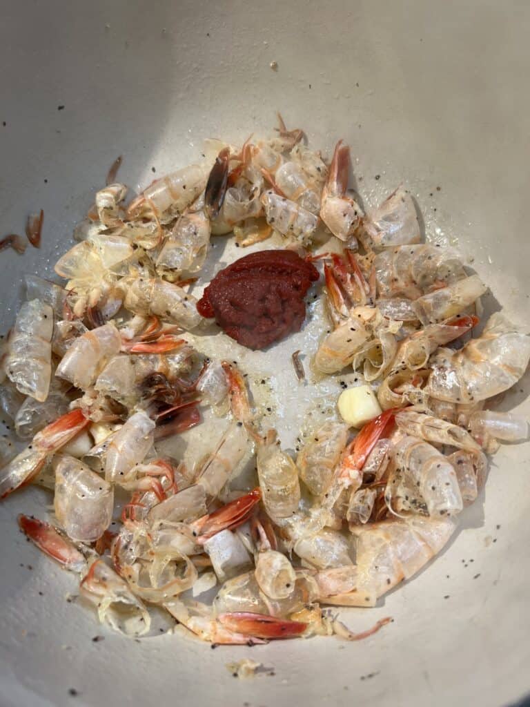 Tomato paste added to a pot with sautéed shrimp shells and smashed garlic.