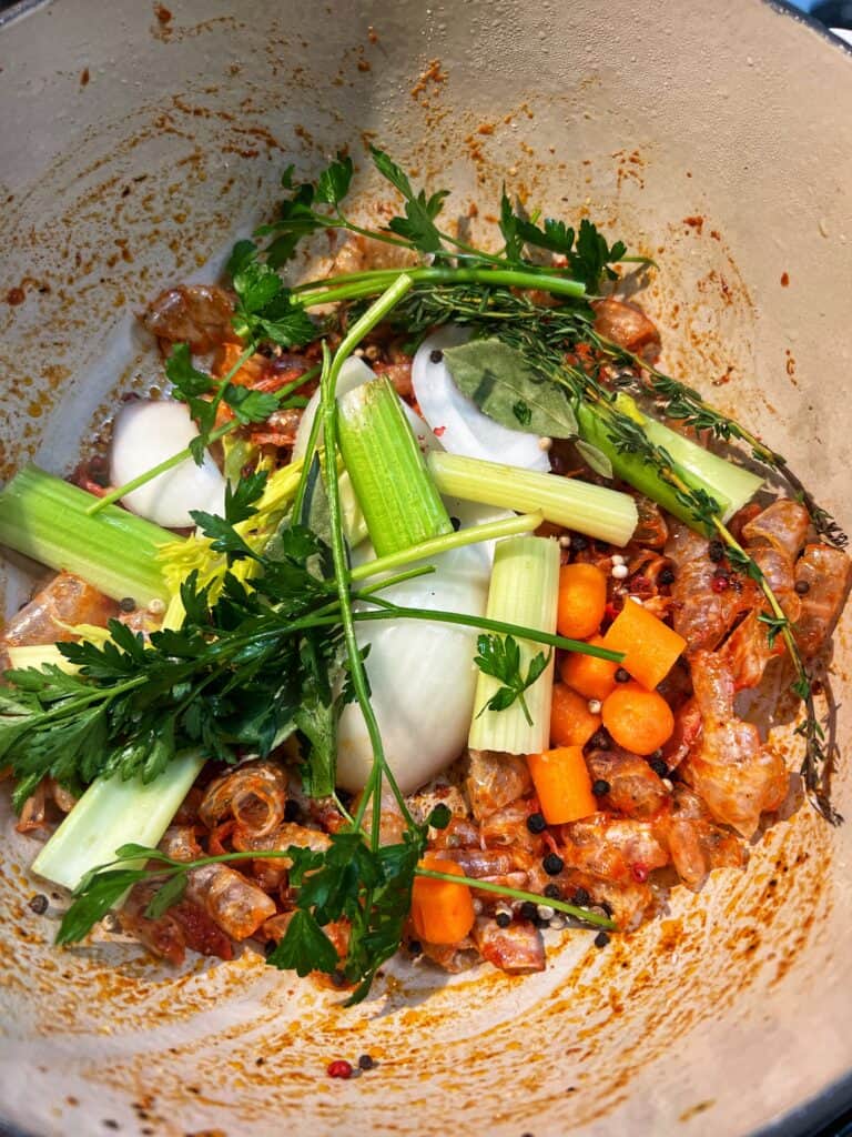 Roughly chopped celery, carrots, onions, fresh thyme sprigs and fresh parsley sprigs added to sautéed shrimp shells with tomato paste in a pot.