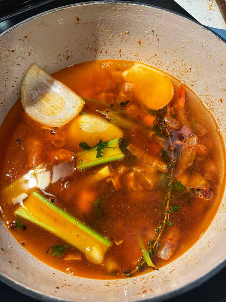 Water added to sautéed vegetables and shrimp shells in a pot.