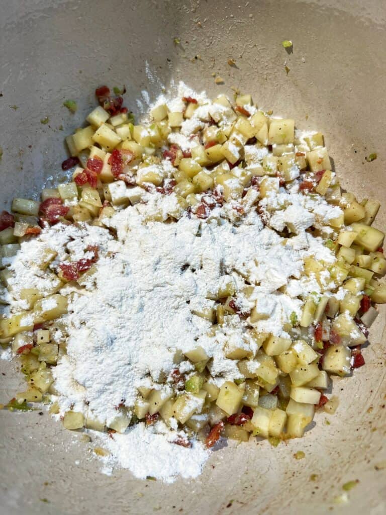 Sautéed vegetables and bacon dusted with flour in a soup pot.
