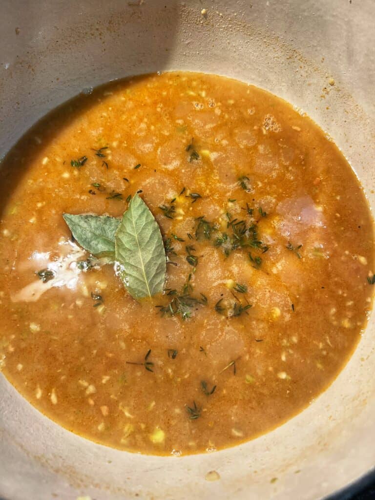Bay leaves and fresh thyme added to shrimp stock in a pot.