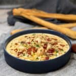 A large blue bowl filled with shrimp and corn chowder with long breadsticks in the background.