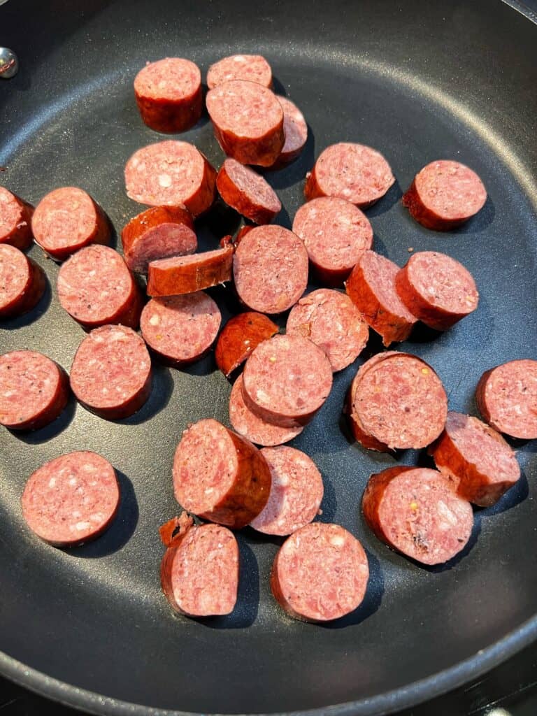 Smoked sausage cut into rounds browning in a non-stick pan.