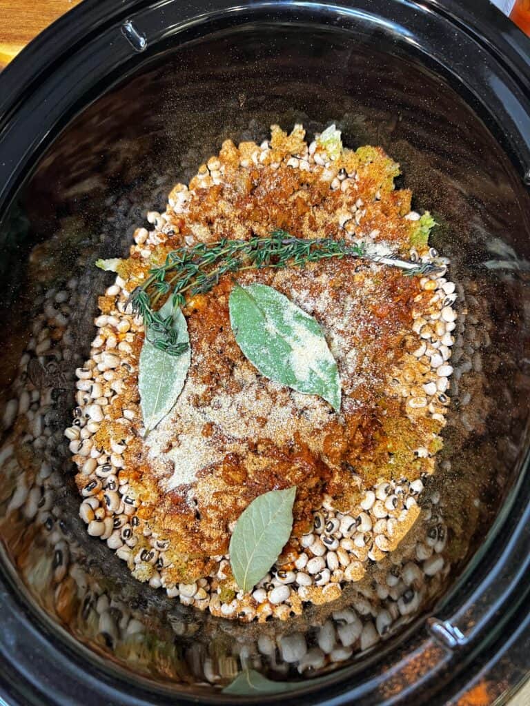 Black-eyed peas in the bottom of a crockpot topped with spices, bay leaves and fresh thyme.