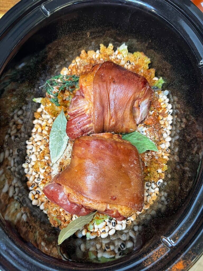Two ham hocks placed into the crockpot with dried black-eyed peas, spices and bay leaves.