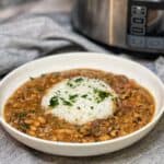 A white bowl with a mound of white rice in the middle and Southern Black Eyed Peas around the rice. All is garnished with fresh chopped parsley.
