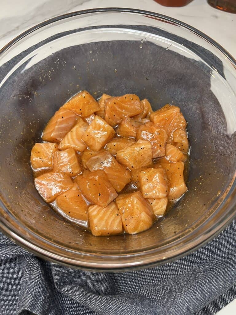 Seasoned salmon bites coated in maple syrup sitting in a glass bowl.