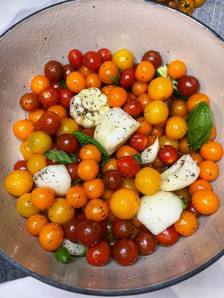 Cherry tomatoes, a quartered yellow onion, a garlic bulb, sliced fresh jalapeño and fresh basil in an enameled cast iron pot.