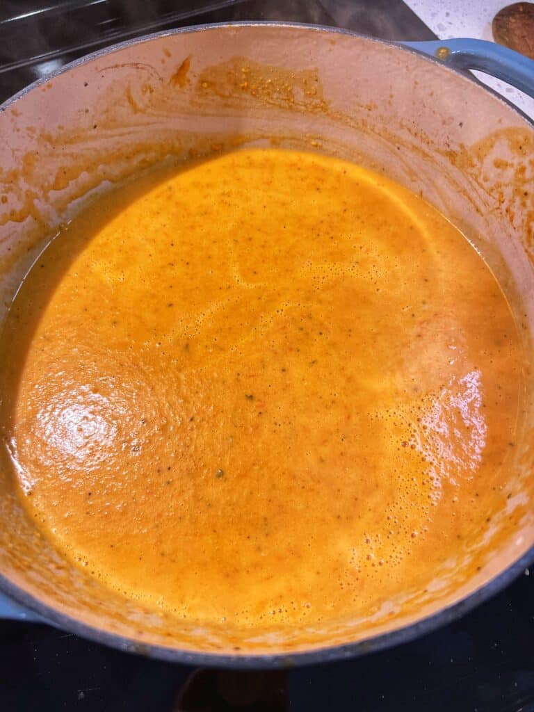 Tomatoes and vegetables blended with heavy cream for roasted tomato basil soup in an enameled cast iron pot.