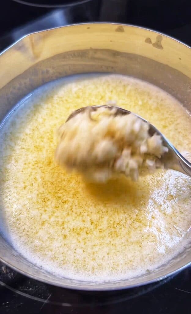 Adding a tablespoon of minced garlic to a small stainless steel pot of melted butter.