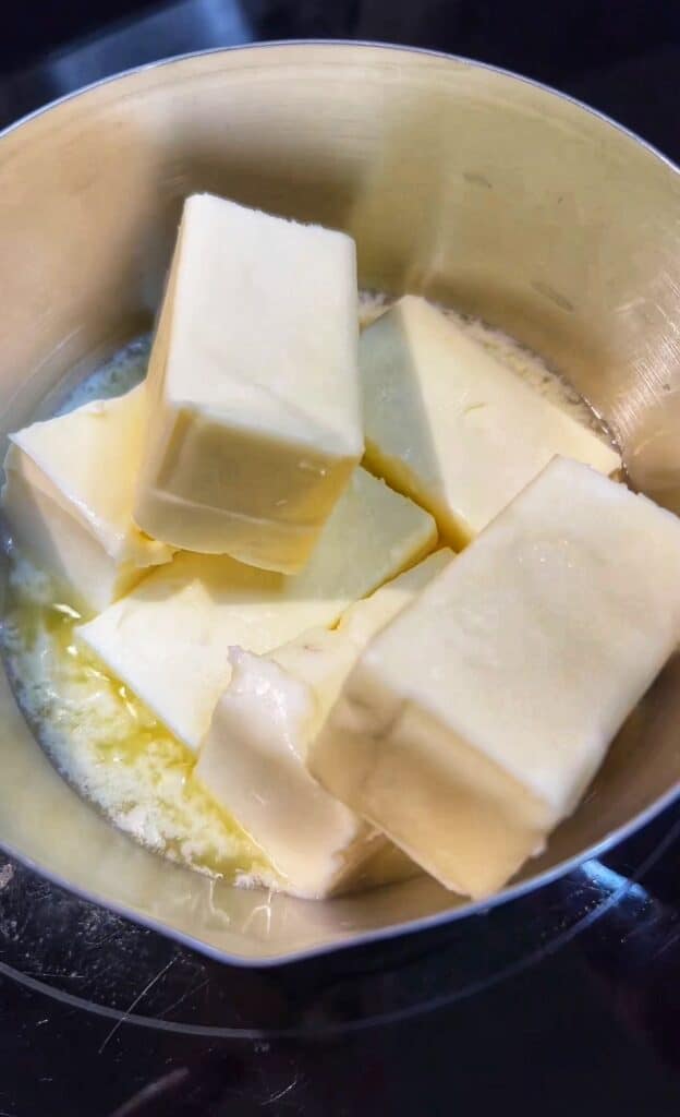 Six half sticks of butter melting in a small stainless steel pot.