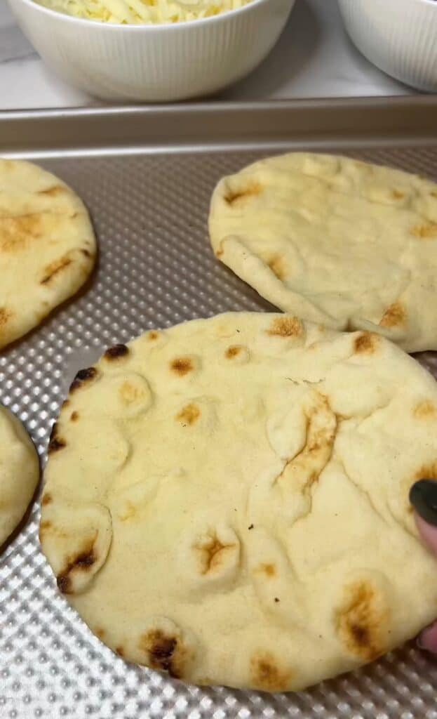 Four pieces of naan on a non-stick baking sheet.