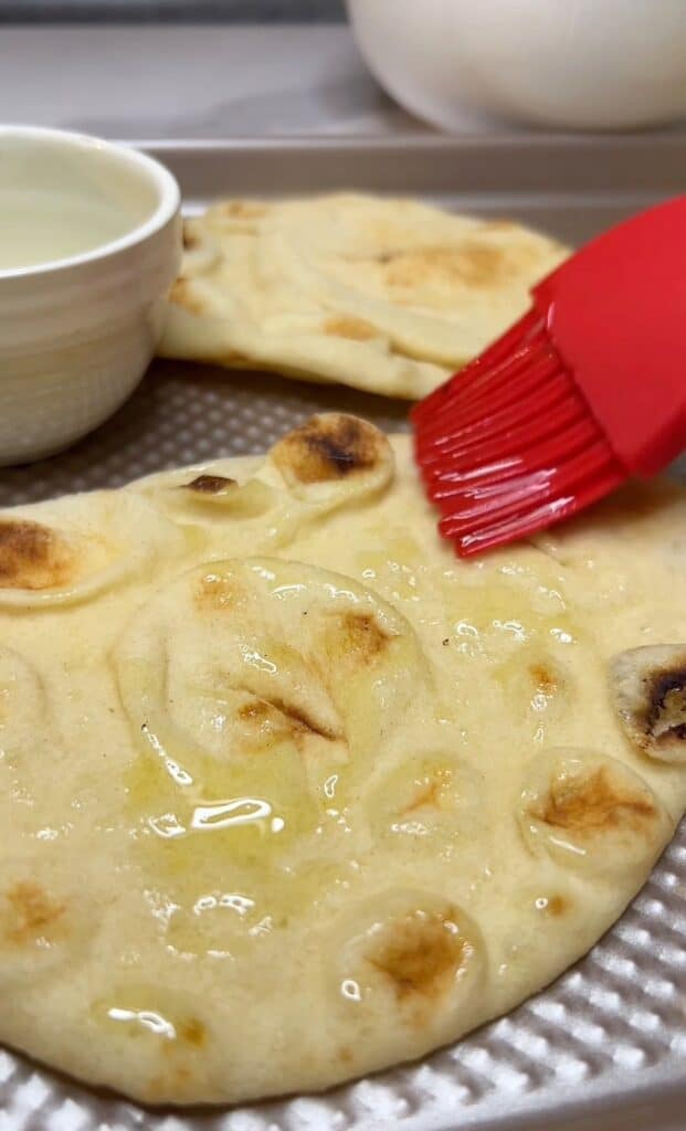 Using a red kitchen brush to brush olive oil onto a piece of naan.