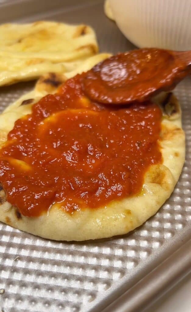 Using a wooden spoon to spoon marinara sauce onto a piece of naan.