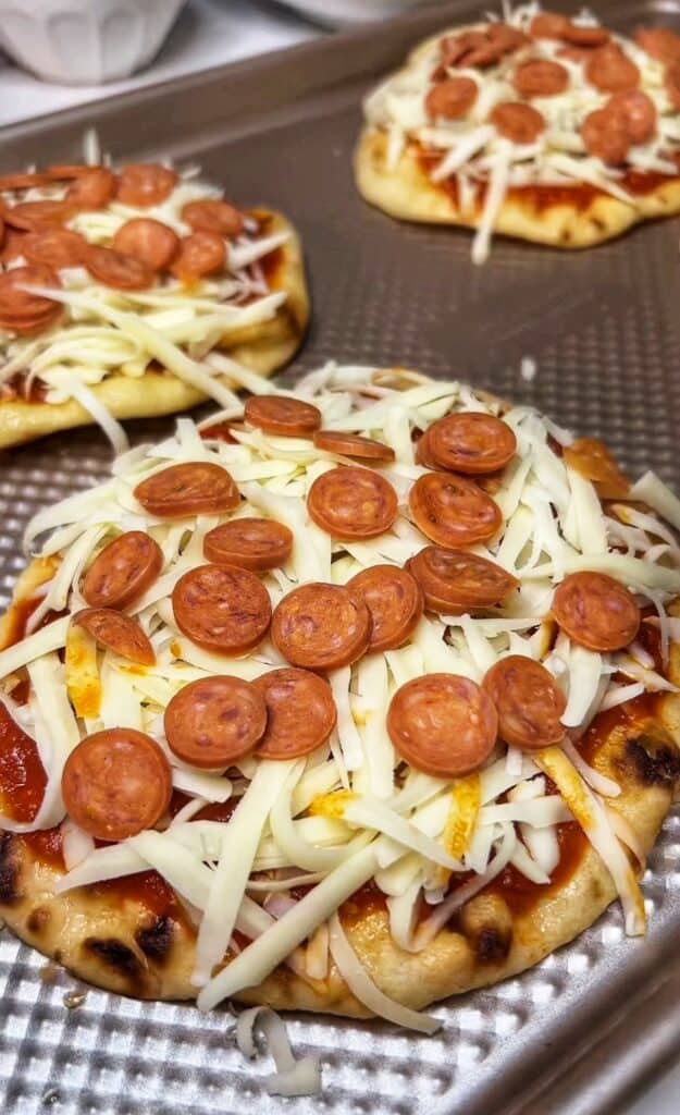 Mini pepperoni added to naan that has been topped with marinara sauce and shredded mozzarella cheese for Naan Pizza.