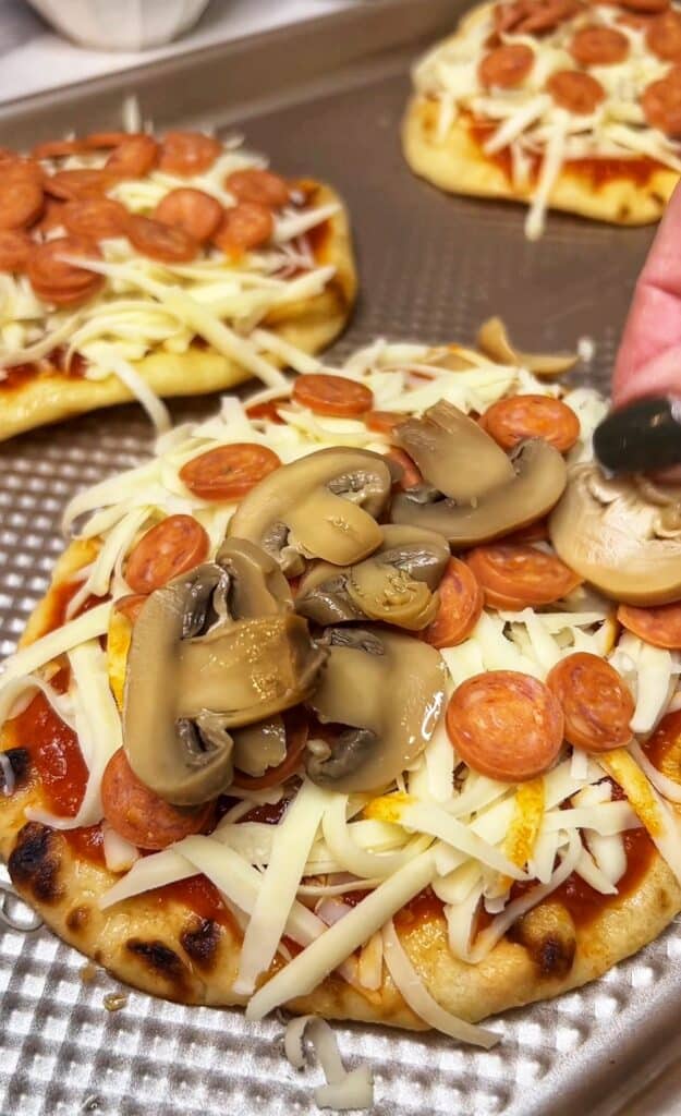 Topping naan pizza with jarred mushrooms.