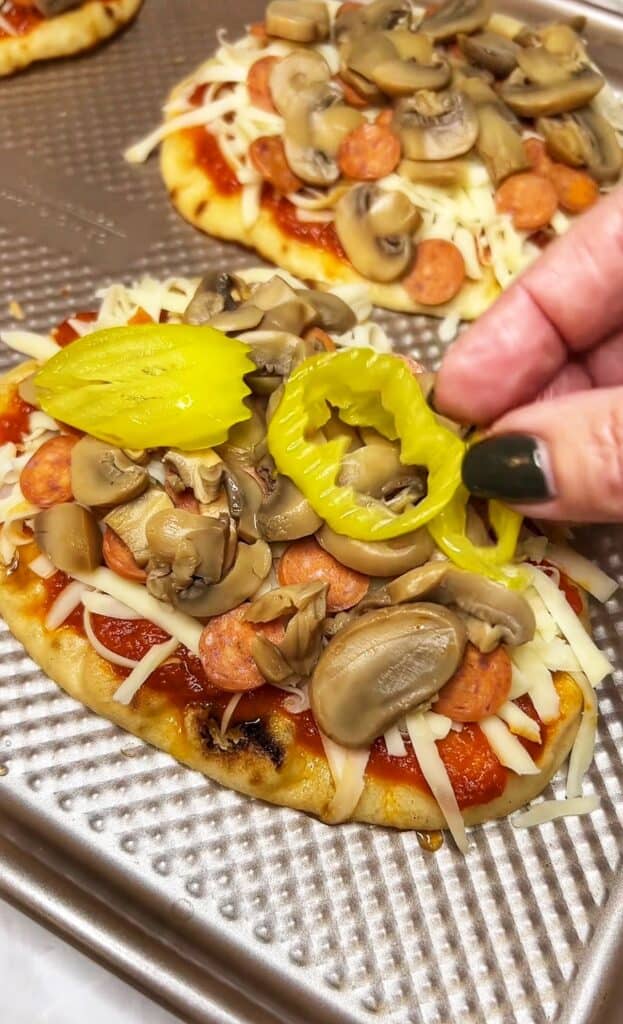 Adding a few sliced banana peppers to a naan pizza that is already topped with cheese, mini pepperoni and jarred mushrooms.