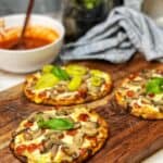 A wooden cutting board holding three naan flatbread pizzas with melted cheese, pepperoni, mushrooms and fresh basil as toppings.