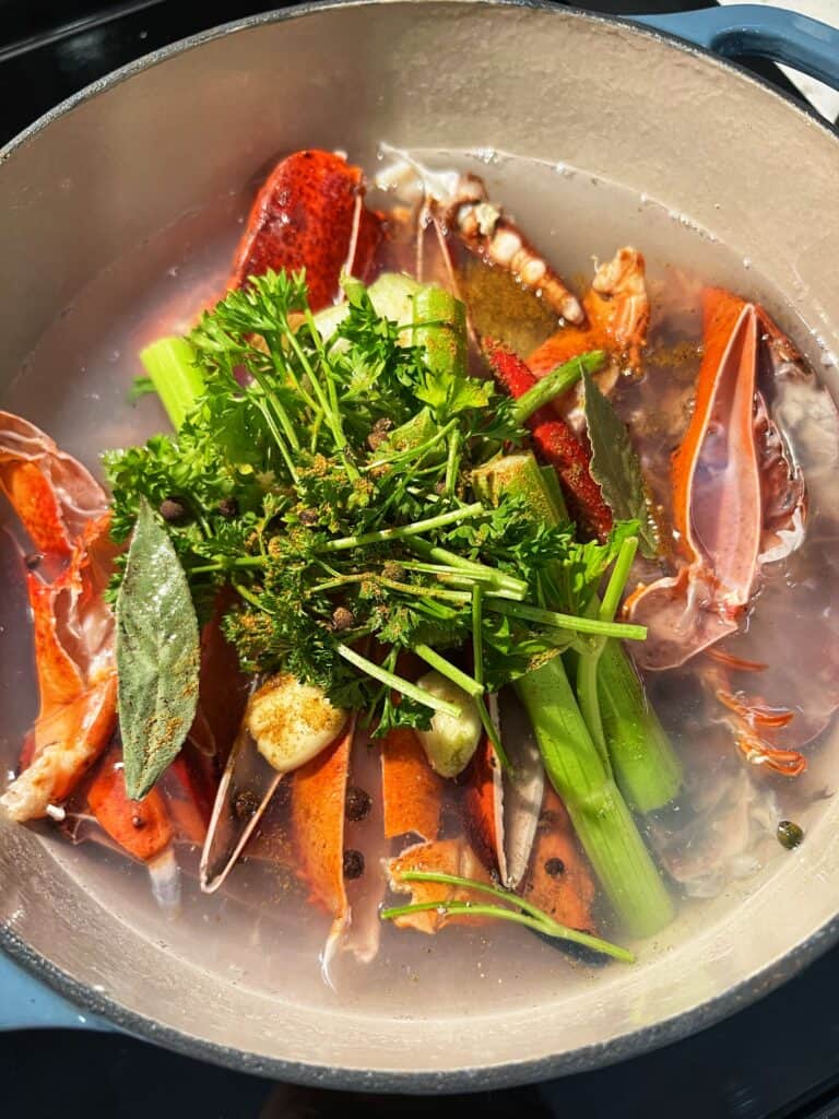 A stock pot full of water, lobster shells, fresh thyme and parsley, onions, smashed garlic cloves, celery and peppercorns for lobster stock.