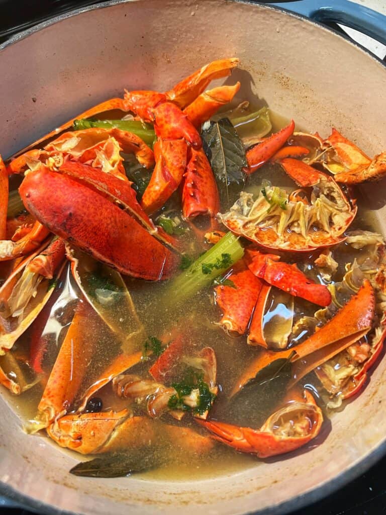 A stockpot of simmered lobster shells, celery stalks, onion, parsley, thyme and bay leaves for rich homemade lobster stock.