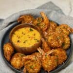 A platter of coconut shrimp garnished with fresh parsley and served with a bowl of creamy sweet chili sauce.
