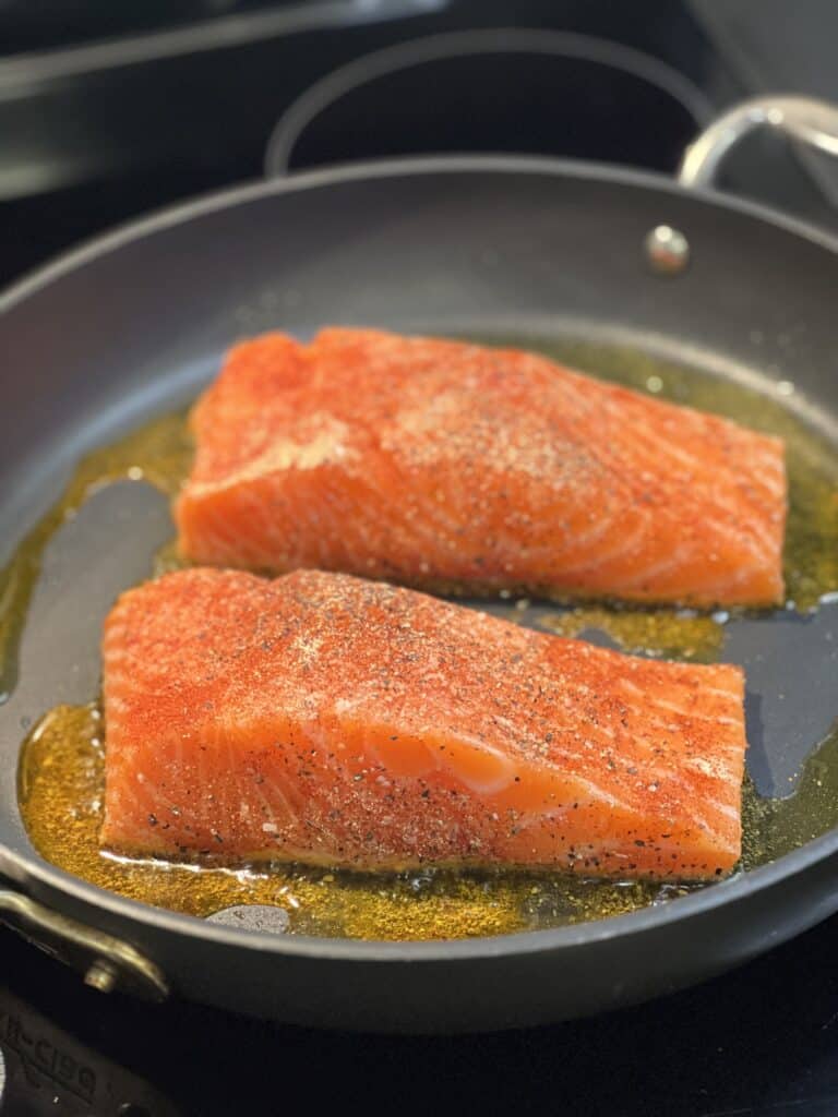 Two filets of salmon starting to sear with a little bit of olive oil in a non-stick pan.