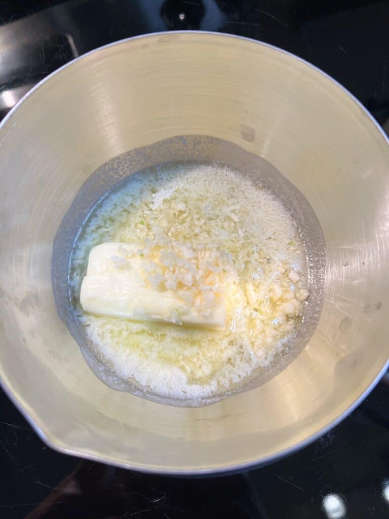 Four tablespoons of butter melting in a small stainless steel pot with minced garlic.