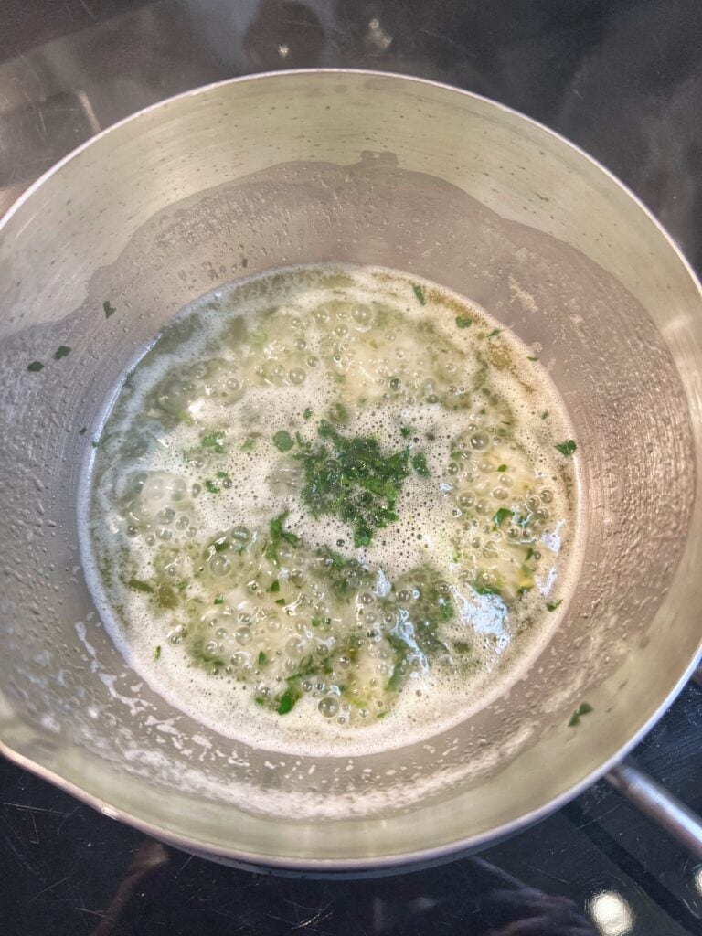 A lemon butter garlic sauce with fresh chopped parsley in a small stainless steel pot.